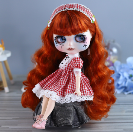 a blythe doll with red hair, blue eyes and a red gingham egl dress and headband. she is sitting on a small rock.