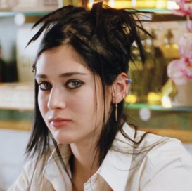 lizzy caplan, a white feminine person with messy black hair, brown eyes with heavy eyeliner and a white shirt with a collar is staring neautrally at the camera.