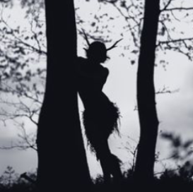 a shadowy satyr figure is standing amongst trees. the image is black and white