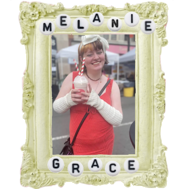 a yellow photo frame holding a picture. the picture if of me, a short femme person with pale skin, split dye hair, and orange strap dress and numerous white accessories smiling as i hold a soda float.