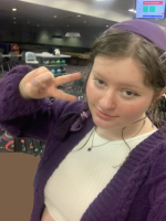 a selfie of melanie, a white feminine person with dark blue eyes and blackish-brown hair with blonde streaks. they are wearing a sligthly sheer lacy white bandana, a golden necklace with a chai charm and a light tan dress with sleves and a v-neck.